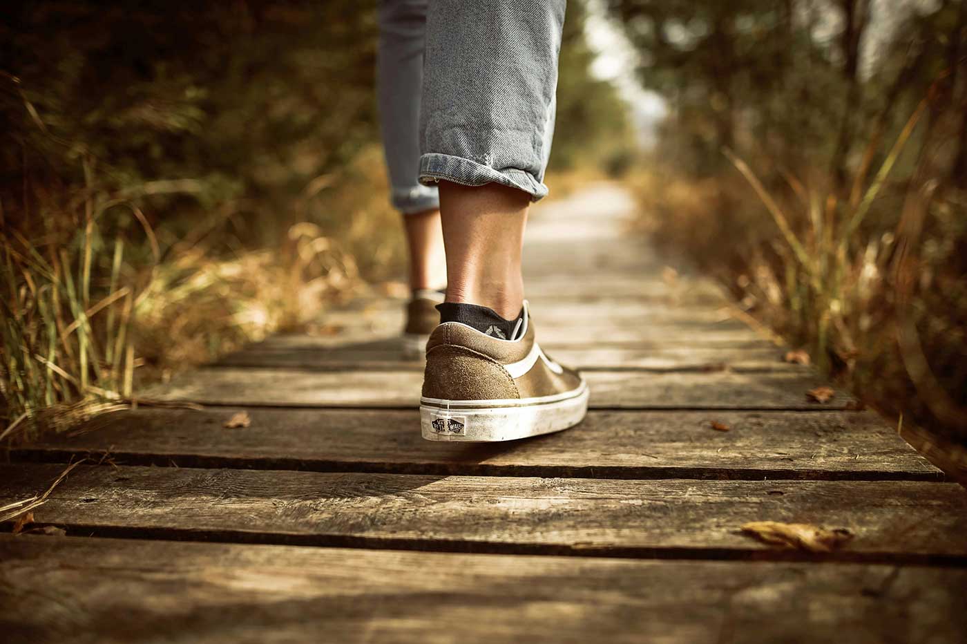 Person wearing sneakers walking along a wooden boardwalk.